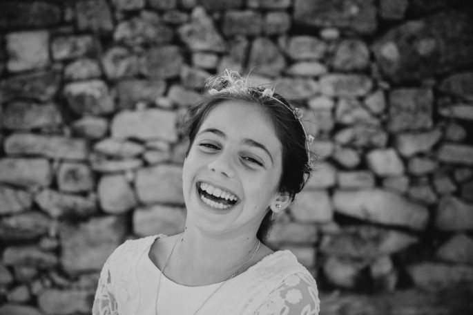 Niña sonriente frente a un muro de piedra.