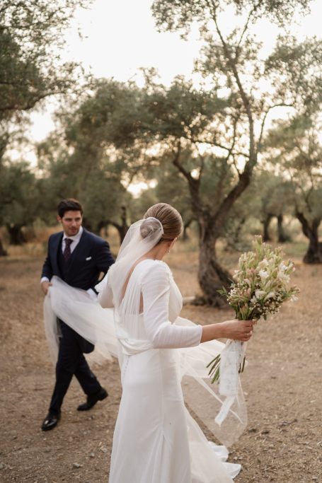 Pareja de novios en un olivar, ella con ramo y velo, él de traje.