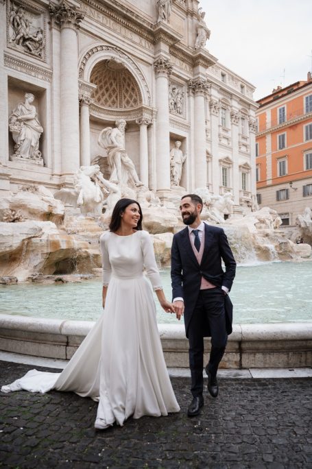 Pareja de novios sonriendo frente a la Fontana di Trevi en Roma.
