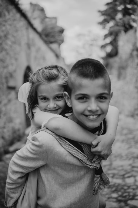 Niño sonriente con una niña montada sobre su espalda, fondo de calle antigua.