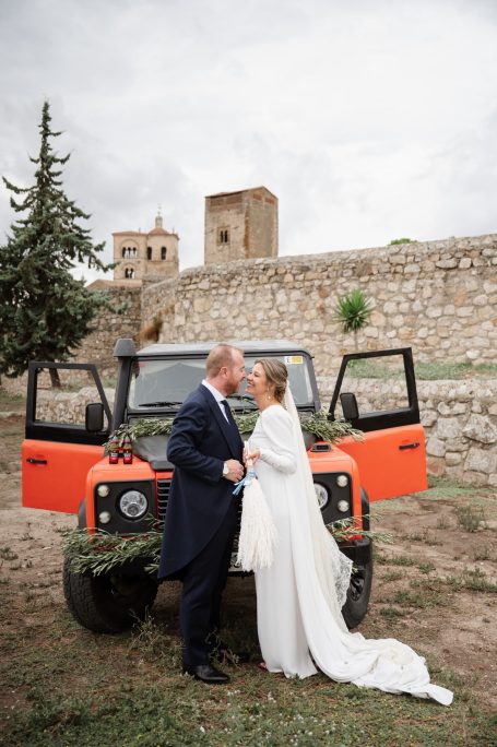 Pareja enamorada posando frente a un vehículo todoterreno en un paisaje histórico.
