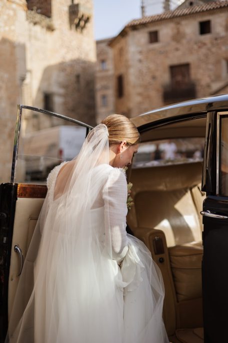 Novia entrando a un coche clásico, vestida con un vestido blanco y velo.