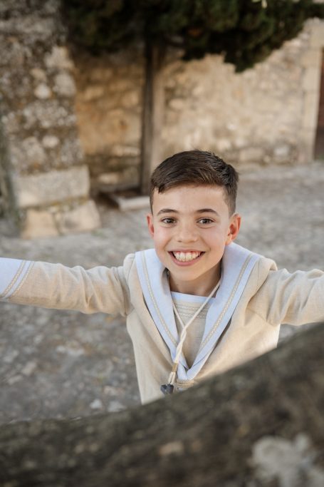 Niño sonriente con brazos extendidos frente a un paisaje rural.
